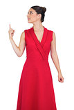 Cheerful glamorous model in red dress pointing up