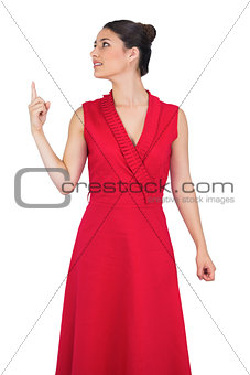 Cheerful glamorous model in red dress pointing up