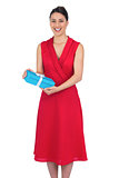 Smiling glamorous model in red dress holding present