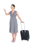 Smiling gorgeous woman carrying her suitcase pointing finger