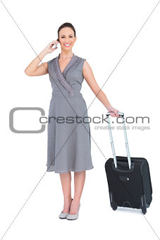 Smiling gorgeous woman carrying her suitcase having phone call
