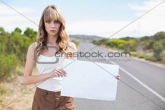 Serious pretty woman holding sign while hitchhiking