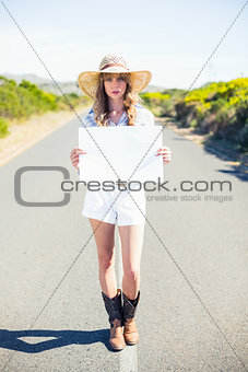 Serious blonde holding sign while hitchhiking on the road