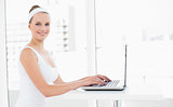 Smiling pretty sportswoman typing on a laptop