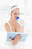 Peaceful pretty sportswoman drinking water while using tablet pc