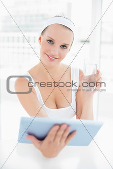 Natural pretty sportswoman holding a glass of water and a tablet pc
