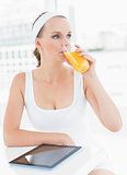 Pensive pretty sportswoman drinking orange juice