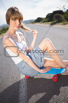 Funky young blonde sitting on her skateboard