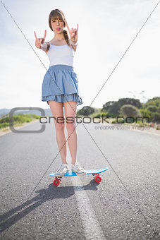 Trendy woman making rock and roll gesture while balancing on her skateboard