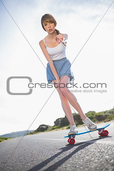 Young woman pointing at camera while balancing on her skateboard