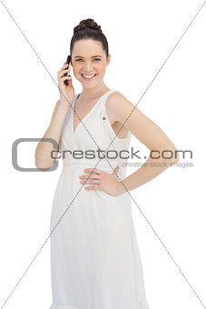 Cheerful young model in white dress having phone call
