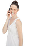 Smiling young model in white dress having phone call