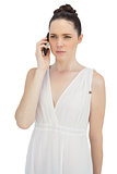Serious pretty model in white dress having phone call