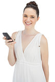 Cheerful pretty model in white dress sending text message
