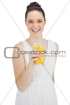 Cheerful model in white dress holding glass of orange juice