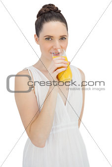 Cheerful model in white dress drinking orange juice