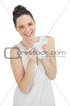 Cheerful model in white dress holding mug of coffee