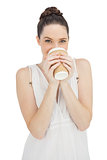 Cheerful natural model in white dress drinking coffee