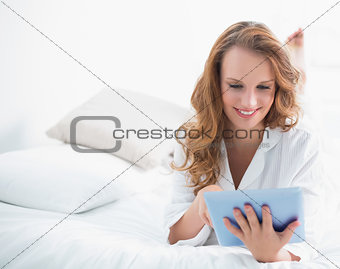 Cheerful pretty woman using a tablet pc lying on her bed