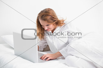 Concentrated pretty woman using a laptop lying on her bed