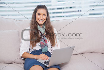 Smiling gorgeous model using laptop sitting on sofa