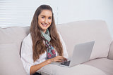 Cheerful gorgeous model using laptop sitting on sofa