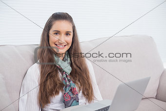 Happy gorgeous model using laptop sitting on sofa