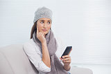 Thoughtful pretty brunette with winter hat on holding her phone