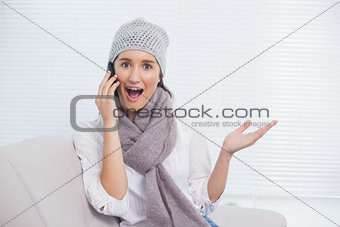 Surprised pretty brunette with winter hat on having a phone call