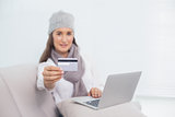 Cheerful pretty brunette with winter hat on holding credit card