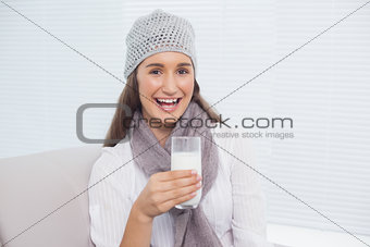 Cheerful pretty brunette with winter hat on holding glass of milk