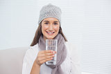 Smiling pretty brunette with winter hat on holding glass of water
