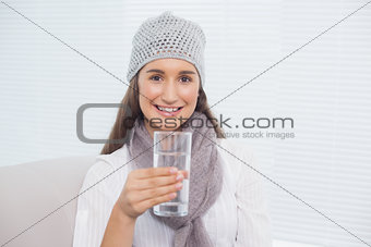 Smiling pretty brunette with winter hat on holding glass of water