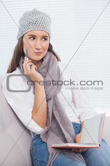 Pensive pretty brunette with winter hat on holding notebook