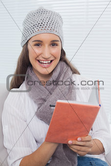 Smiling pretty brunette with winter hat on writing on notebook