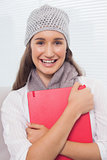 Smiling brunette with winter hat on holding folder