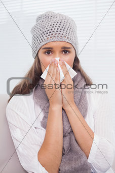Pretty brunette with winter hat on blowing her nose