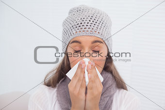 Cute brunette with winter hat on blowing her nose