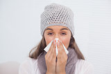 Sick brunette with winter hat on blowing her nose