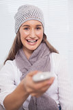 Smiling brunette with winter hat on holding remote