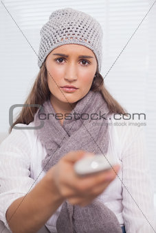 Serious brunette with winter hat on holding remote