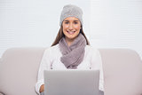 Smiling brunette with winter hat on using her laptop