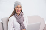 Happy brunette with winter hat on using her laptop