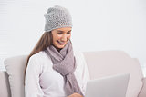 Cheerful cute brunette with winter hat on using her laptop