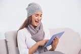 Cheerful cute brunette with winter hat on scrolling on her tablet