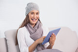 Smiling cute brunette with winter hat on scrolling on her tablet