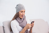 Astonished cute brunette with winter hat on using her smartphone