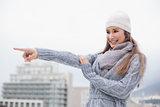 Smiling cute brunette with winter clothes on pointing away