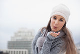 Pretty brunette with winter clothes on sending an air kiss to camera