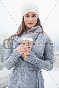 Peaceful pretty brunette with winter clothes on holding coffee
